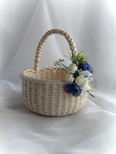 a wicker basket with flowers in it sitting on a white cloth covered tablecloth