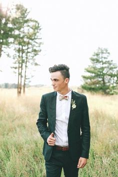 a man in a suit and bow tie standing in tall grass