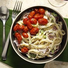 a bowl filled with pasta and tomatoes on top of a green place mat next to silverware