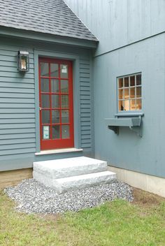 a red door is on the side of a blue house with steps leading up to it