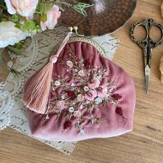 a pink purse sitting on top of a wooden table next to flowers and a pair of scissors