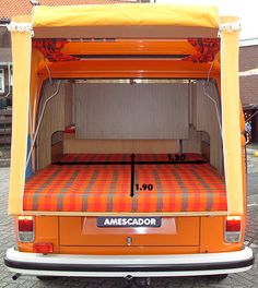 an orange and white bed in the back of a van with its door open to show it's size