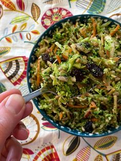 a person holding a fork in a bowl filled with broccoli and raisins