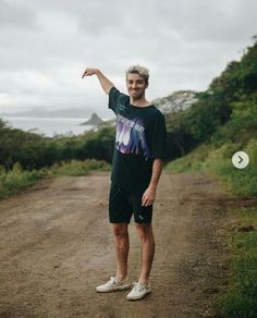 a man standing in the middle of a dirt road pointing at something with his hand