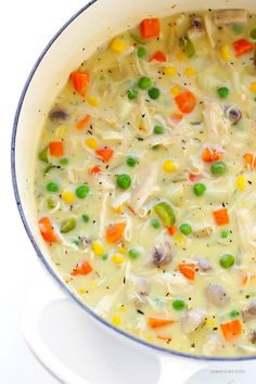 a pot full of soup with carrots, peas and other veggies in it