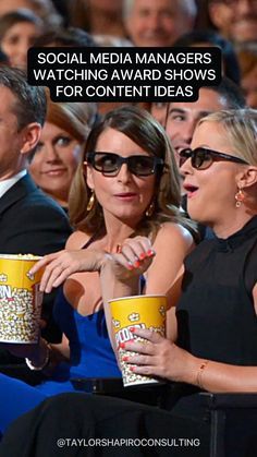 two women sitting next to each other in front of an audience with popcorn cups on their laps