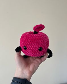 a hand holding up a pink knitted object in the shape of a crab with black eyes