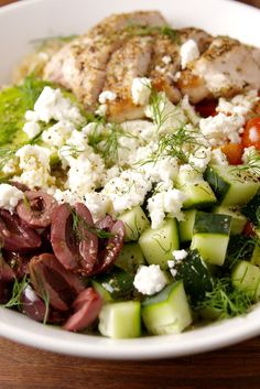 a white bowl filled with meat, vegetables and feta cheese on top of a wooden table