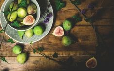 a bowl filled with green figs on top of a wooden table next to other fruit