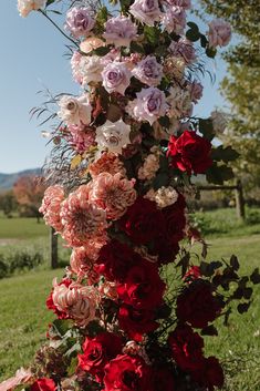 a bunch of pink and red flowers on a pole in the grass by some trees