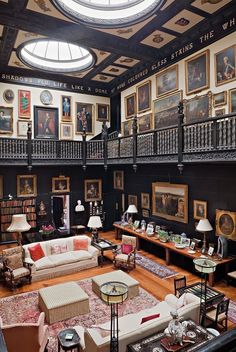 a large living room filled with furniture and paintings on the walls, along with high ceilings