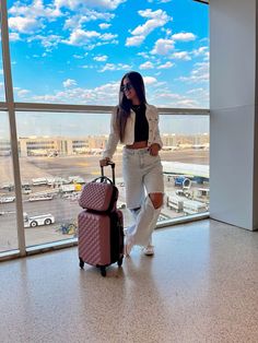 a woman is pulling two suitcases in an airport terminal while looking out the window