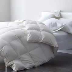 an unmade bed with white comforters and pillows on top of it in a room