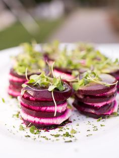 beets are arranged on a white plate with sprouts and seasoning around them