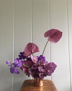 purple flowers are in a vase on a wooden table next to a white painted wall