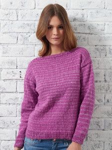 a woman standing in front of a white brick wall wearing a purple sweater and jeans