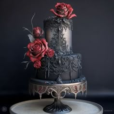 a three tiered black cake with red roses on top and an intricately decorated stand