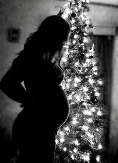 a pregnant woman standing in front of a christmas tree