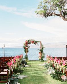 an outdoor ceremony set up with chairs and flowers on the grass, overlooking the water