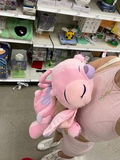 a woman holding a pink stuffed animal in her arms while standing next to shelves filled with toys