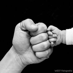 a black and white photo of a baby holding an adult's hand