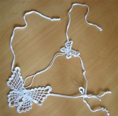 two white crocheted necklaces sitting on top of a wooden table