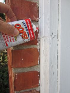 a hand is holding a can of spray paint near a brick wall that has been painted white