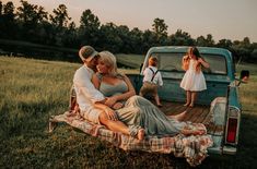 a man and woman sitting on the back of an old pickup truck with their children