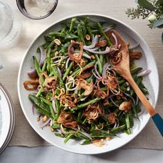 a white bowl filled with green beans and onions on top of a table next to silverware