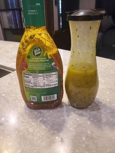 a bottle of mustard sitting next to a glass on a counter top with a container in the background