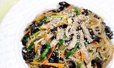 a white plate topped with noodles and veggies covered in sesame seed seeds on top of a table