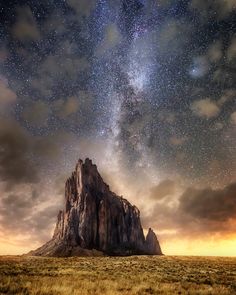 the night sky is filled with stars above a rocky outcropping in an open field