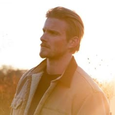 a man standing in a field with the sun shining on him and looking off into the distance