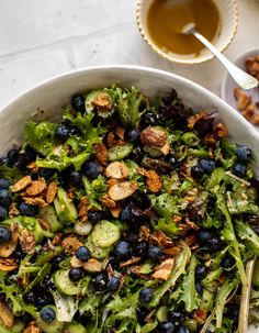 a white bowl filled with blueberries, cucumbers and nuts next to a spoon