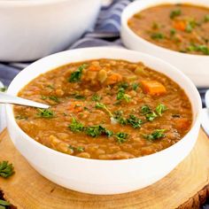 two white bowls filled with lentula soup on top of a wooden cutting board and garnished with parsley