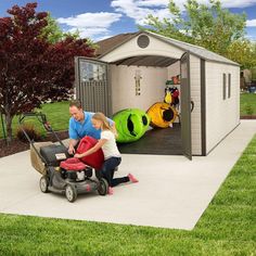 a man pushing a child in a lawn mower next to a shed with kayaks