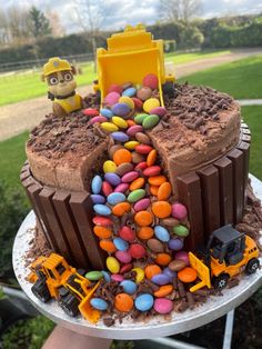 a birthday cake with chocolate frosting, candy and construction vehicles on it's side