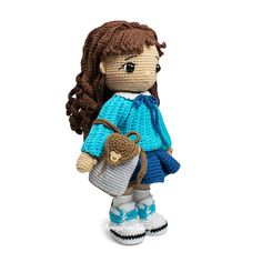 a crocheted doll with brown hair and blue dress is holding a small purse