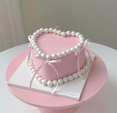 a pink heart shaped cake with pearls on it's sides and a ribbon around the edge