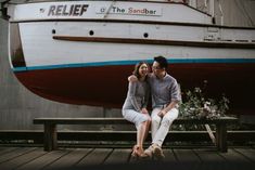 two people sitting on a bench in front of a boat