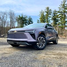 a silver chevrolet suv parked on top of a gravel road next to trees and bushes