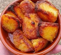 a hand holding a bowl filled with fried potatoes