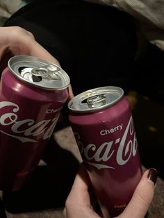 two coca - cola cans are being held by someone