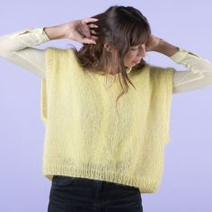 a woman wearing a yellow sweater and black pants with her hands on her head,