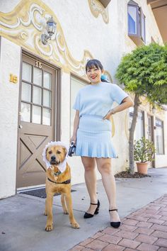 a woman standing next to a brown dog on a brick sidewalk in front of a building