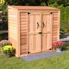 a large wooden storage shed with two doors on the side and flowers in the background