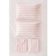 the pink and white bedding is neatly made with two pillows, one has an orange stripe