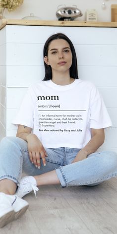 a woman sitting on the floor with her legs crossed wearing mom t - shirt and jeans