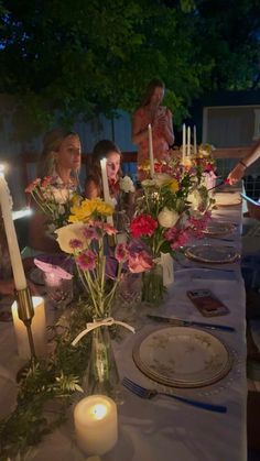 a group of people sitting at a table with flowers and candles