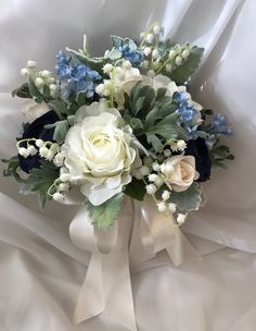 a bridal bouquet with blue and white flowers on a white satin bed sheet,